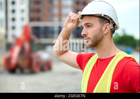 Serene bearded construction worker touching his protective helmet Stock Photo