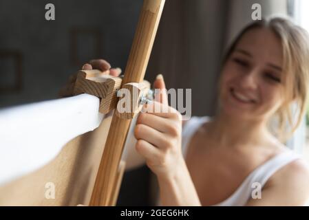 close-up of the hands of a woman artist in an art studio stands near the easel and fixes the canvas. . Stock Photo