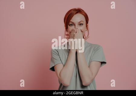 Excited happy red-haired woman covering mouth with hands, looking with surprised facial expression Stock Photo