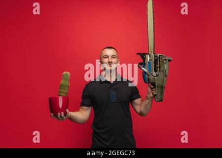 One young caucasian man with cactus and electric saw posing over red background. Stock Photo