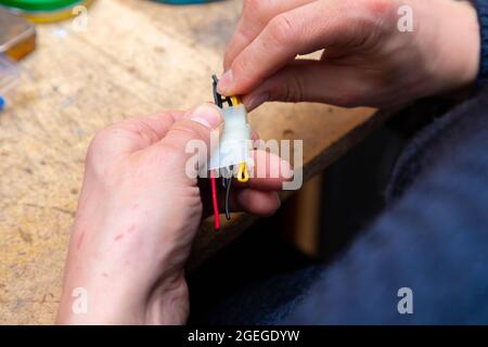 Young man's hands hold multicolored wires over desk with tools Stock Photo