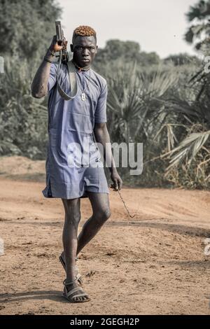 A man looked straight into the camera as he walked past, holding his gun casually behind his back. TEREKEKA, SOUTH SUDAN: In one image, a man stared i Stock Photo