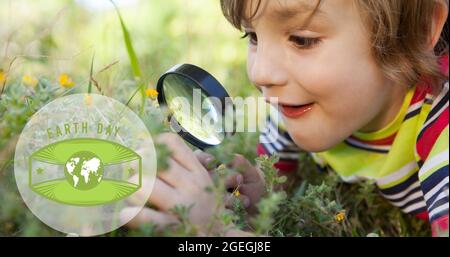 Composition of green globe logo and earth day text over boy using magnifying glass in nature Stock Photo