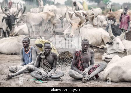 Three tribe members looked into the camera as they sat by a burning fire. TEREKEKA, SOUTH SUDAN: In one image, a man stared into the camera surrounded Stock Photo