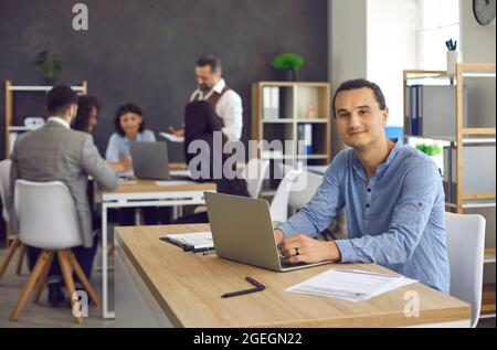 Young smiling office worker is typing on a laptop, working on a project Stock Photo