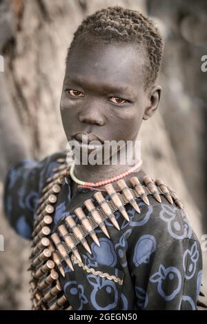 A man wore machine gun bullet rounds across his shoulders. TEREKEKA, SOUTH SUDAN: In one image, a man stared into the camera surrounded by cows while Stock Photo