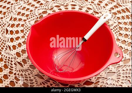 Empty red plastic bowl with egg whisk. Crochet tablecloth background. Top view. Closeup. Stock Photo