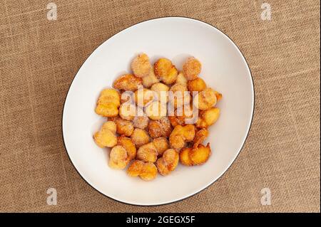 Delicious and traditional homemade Brazilian sweet called "Bolinho de Chuva" on a plate. Isolated on jute background. Top view. Copy space. Stock Photo