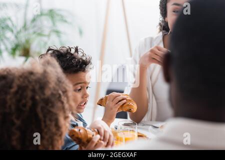 excited african american boy holding croissant near blurred family Stock Photo