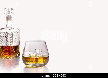 A glass decanter half filled with cognac or other alcoholic beverage and a glass with ice isolated on a white background. Copyscape Stock Photo