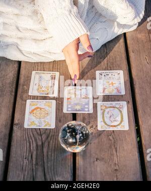 Woman's hand with purple nails points to five Tarot cards spread out on wooden surface next to crystal ball. Vertical. Minsk, Belarus - 07.28.2021 Stock Photo