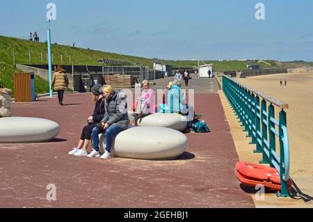 WHITLEY BAY. TYNE and WEAR. ENGLAND. 05-27-21. The Promenade with people seated on large pebble shapes seats. Stock Photo