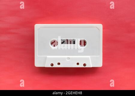 One white compact audio cassette tape with empty label isolated on red background. Top down view flat lay with empty space for text Stock Photo