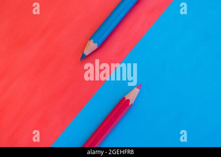 Pink and blue background divided diagonally with two matching colored pencils placed on opposite colors. Top down view flat lay with space for text Stock Photo