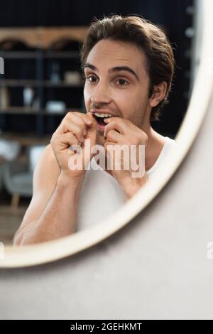 young man cleaning teeth with dental floss near mirror Stock Photo