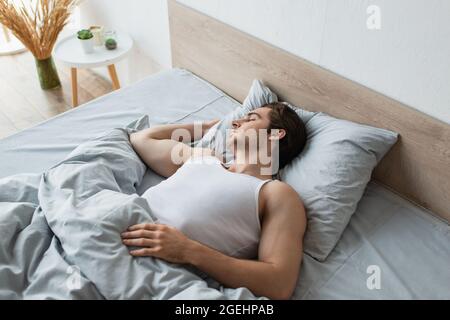 young brunette man sleeping in bed under blue blanket Stock Photo