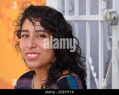 Beautiful positive emotional young Mexican Latina Hispanic woman with wet long black curls poses in front of a white security steel window grill. Stock Photo