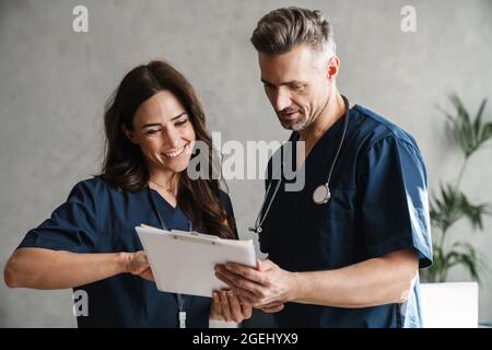 Two smiling doctors in medical uniforms discussing patient anamnesis together, considering test results indoors Stock Photo