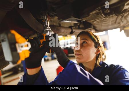 Mixed race female car mechanic wearing overalls, using screwdriver Stock Photo