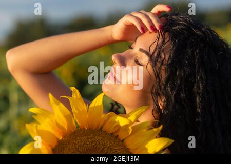 Close-up portrait of a young woman looking out from behind a large sunflower. Summertime concept. Stock Photo