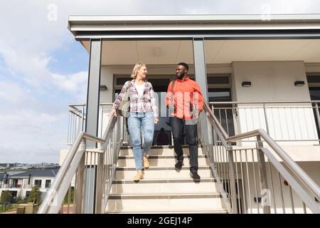 Smiling diverse female and male colleagues walking downstairs outside office and talking Stock Photo