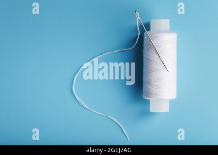 A skein of white thread with a needle on a blue background. Free space Stock Photo