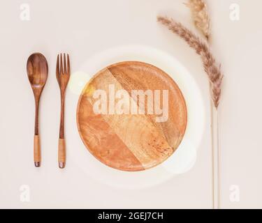 Eco friendly, minimalistic, horizontal composition with trendy serving with empty wooden plate, wooden spoon, fork and dry flowers on a beige backgrou Stock Photo