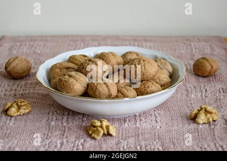 Walnuts in white plate on table covered with beige napkin, close-up, selective focus. Stock Photo