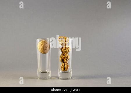 Walnut and walnut kernels are placed in two glass cylindrical glasses on a gray background. Close-up. Selective focus. Copy space. Stock Photo