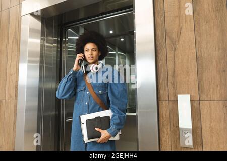Serious african american female business creative using smartphone and holding notebooks Stock Photo