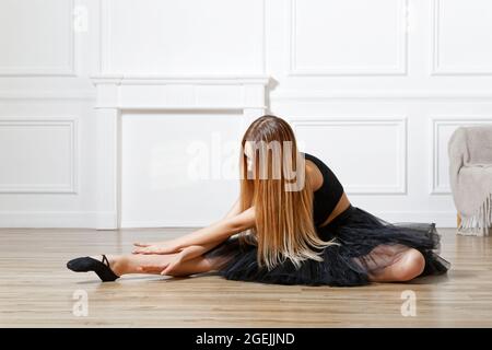 Young ballerina stretching her leg in dance studio. Woman doing