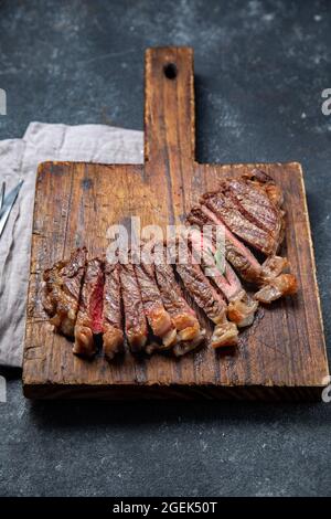 Fried strip loin steak on wooden board, black background. Top view Stock Photo