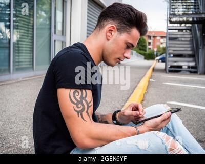 Young man using tablet PC sitting on street curb Stock Photo