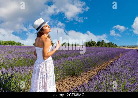 Woman with closed eyes sniffing lavender flowers. Concept of summer and wellness in nature. Copy space for your message. Stock Photo