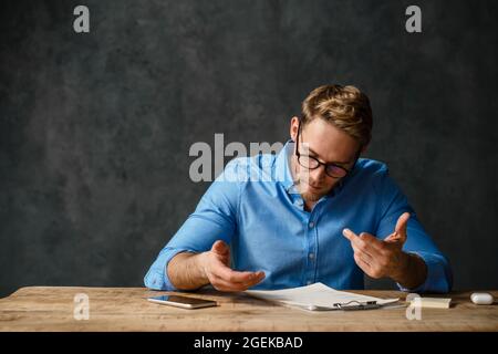 Frowning business man working with documents while sitting at the desk isolated over black background Stock Photo