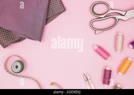 Pink background with sewing accessories and fabric. Sewing threads, needles, fabric, sewing centimeter or measuring tape. Top view, copy space. Tailor Stock Photo