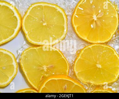 Lemon close-up in liquid with bubbles. Slices of yellow ripe lemon in water. Close-up fresh slices of lemon on white background Stock Photo