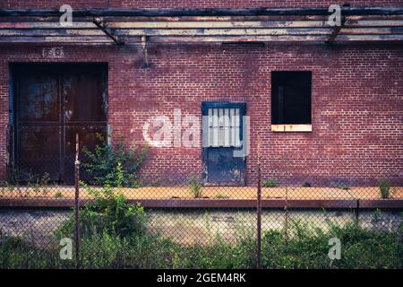 Old factory doors set in brick wall on abandoned loading dock with chainlink fence in foreground Stock Photo