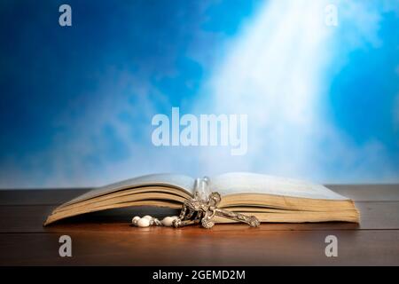 Dramatic image showing a bright light beam shining on an old bible with a rosary laying in front of it. Stock Photo