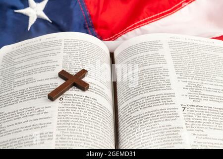 A small wooden cross rests on a bible with the American flag on the table. Stock Photo