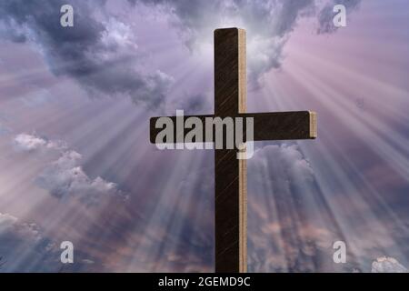 Dramatic image showing a religious church cross framed against a moody sky that is beginning to open and pierce light through behind the cross, showin Stock Photo