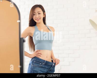 Young woman in jeans large size and standing in front of mirror. Weight Loss concept Stock Photo