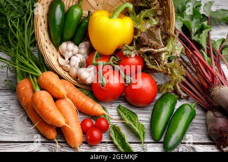 Assorted vegetables and basil in a basket on a wooden table. Stock Photo