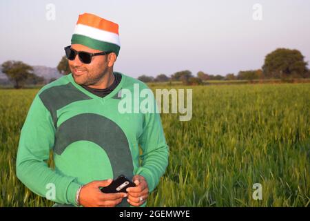 Wearing a tricolor turban, an Indian farmer is talking on his mobile in the evening in his wheat fields, with glasses Stock Photo