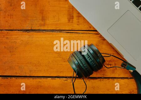 Top view of wireless headphones and part of laptop keyboard. Modern gadgets on wooden table. Copy space for advertising. Working space. Stock Photo