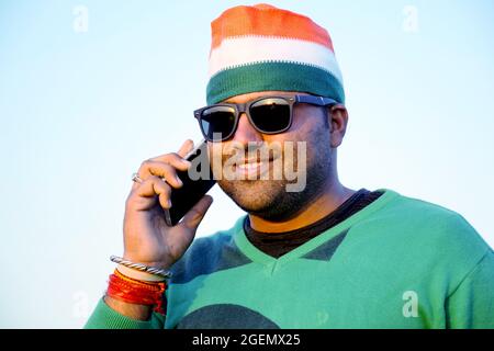 Wearing a tricolor turban, an Indian farmer is talking on his mobile in the evening in his wheat fields, with glasses Stock Photo