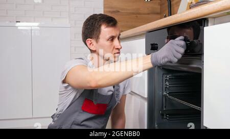 Man checks broken oven to repair siting on floor in kitchen Stock Photo