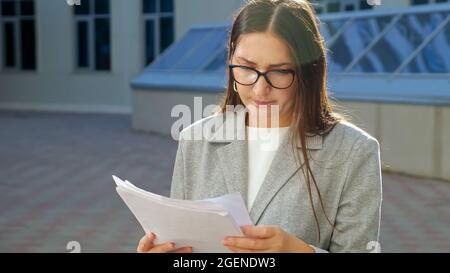 young woman in a formal suit and glasses with a serious face examines documents on the street Stock Photo