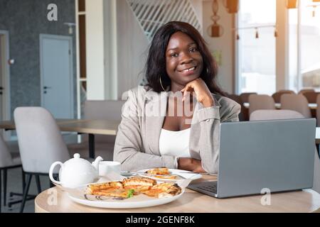 african american woman in business suit with laptop and pizza in cafe Stock Photo