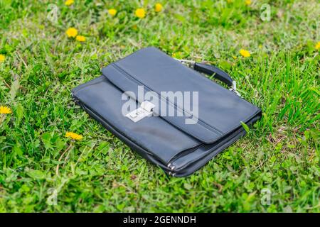 Lost leather briefcase with a combination lock lies in the grass on the lawn in the park in summer Stock Photo